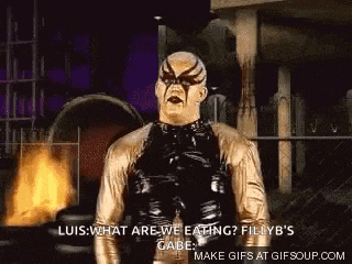 a man in a gold and black costume is standing in front of a fire and talking to another man .
