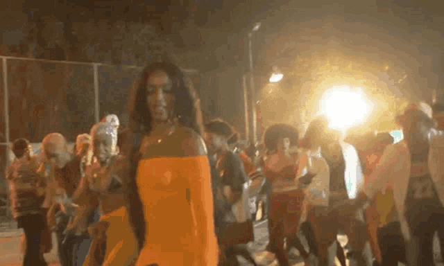 a woman in an orange dress is standing in front of a crowd of people .