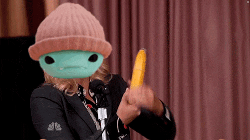 a woman wearing a beanie and a mask holds a banana