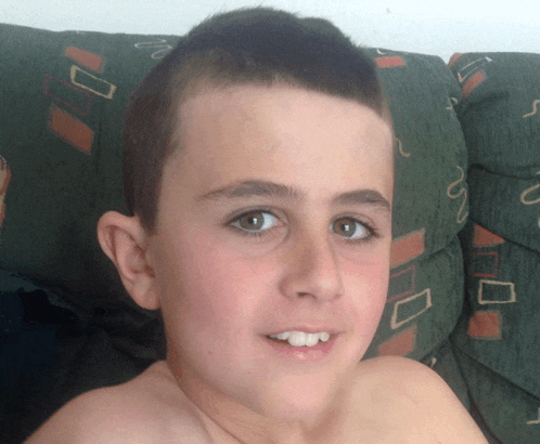 a young boy without a shirt sits on a couch