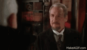 a man in a tuxedo and bow tie is talking to another man in a suit and tie .