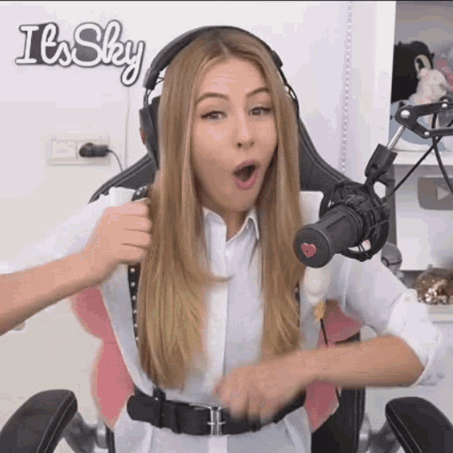 a woman wearing headphones is sitting in a chair in front of a microphone with her mouth open .