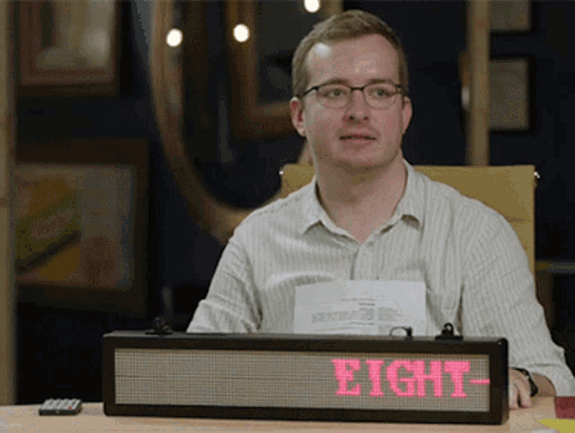 a man sits at a desk with a sign that says eight on it