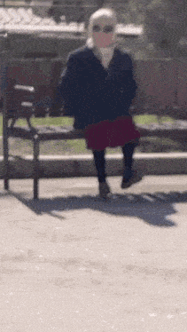 a woman wearing a mask and sunglasses is sitting on a park bench .