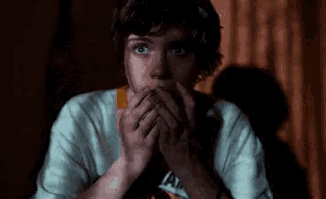 a young boy is covering his mouth with his hands in a dark room .