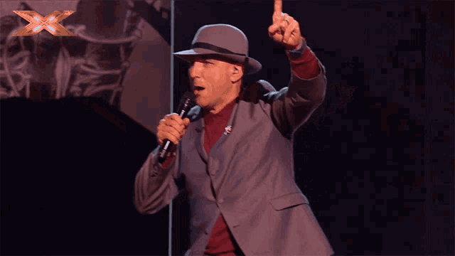 a man singing into a microphone with a x on the bottom right