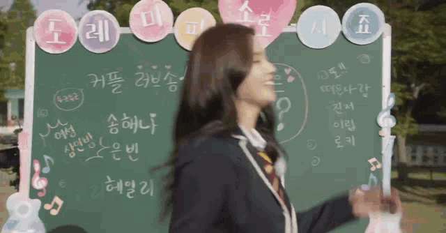 a girl in a school uniform is standing in front of a blackboard with chinese writing on it