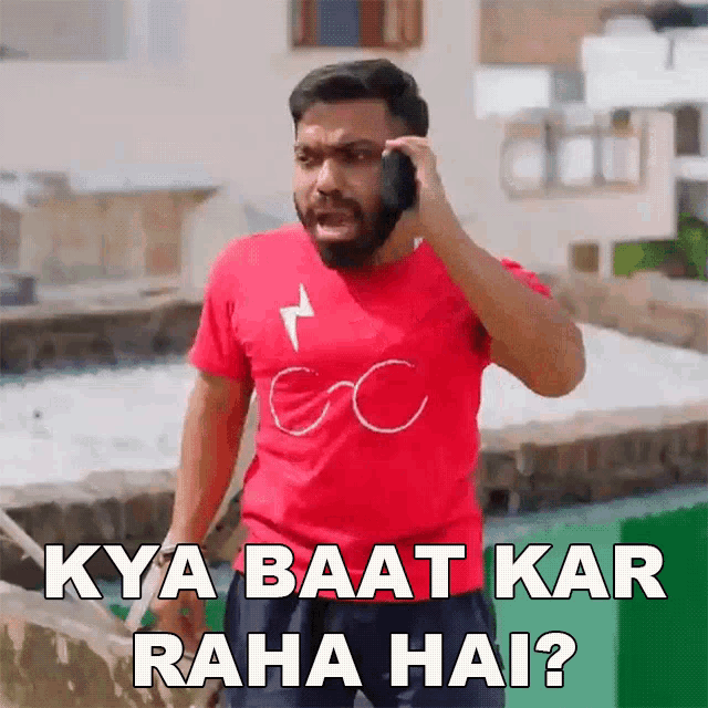 a man in a red shirt is talking on a cell phone with the caption kya baat kar raha hai ?