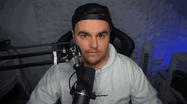 a man sitting in front of a shure microphone looks at the camera