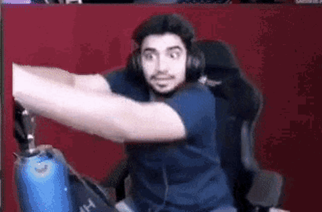 a man wearing headphones and a blue shirt is sitting in a gaming chair .
