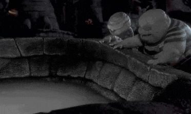 a black and white photo of a nightmare before christmas scene with two ghosts standing next to a well .