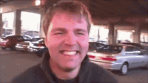 a man is smiling in front of a parking lot with cars parked behind him .