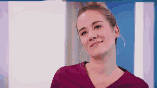 a woman in a purple scrub top is smiling in front of a blue door .