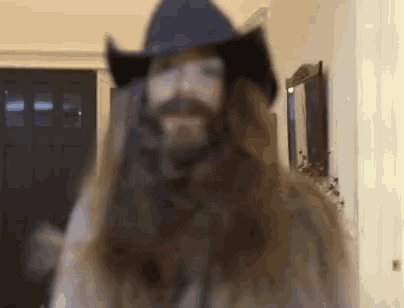 a man with long hair and a beard is wearing a cowboy hat and glasses .