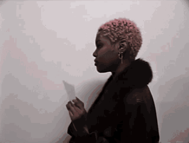 a woman with pink hair is standing in front of a white wall holding a piece of paper .