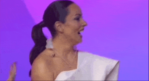 a woman in a white dress is standing in front of a purple background with her mouth open .