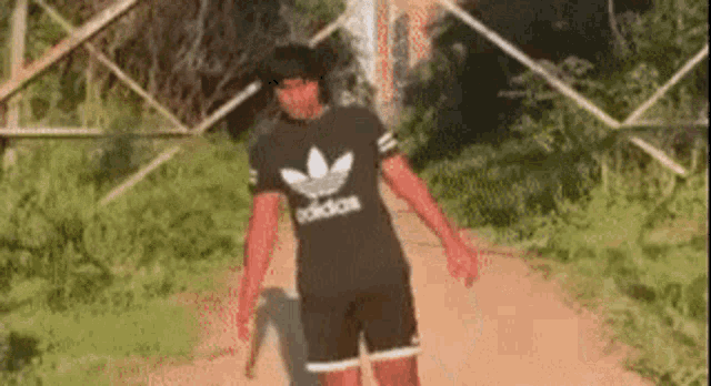 a person wearing a black adidas shirt and shorts is walking down a path .