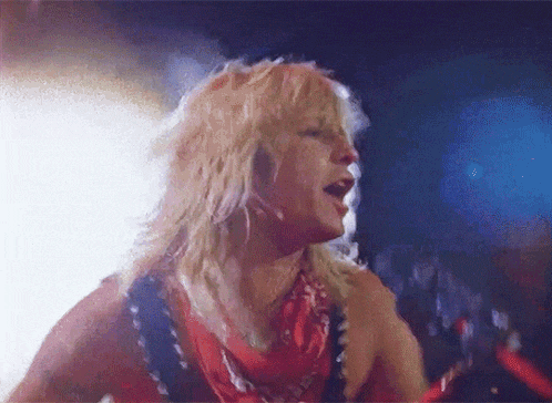 a man with blonde hair and a red scarf around his neck is singing