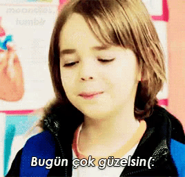 a young girl says " bugun çok güzelsin " in front of a poster of a heart