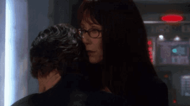 a woman wearing glasses is hugging a man .