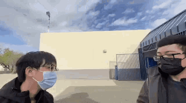 two men wearing masks and glasses are standing next to each other in front of a building .