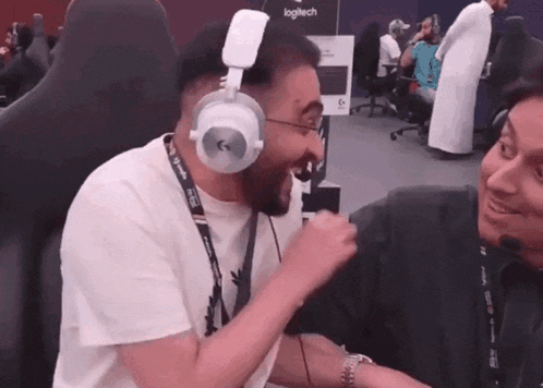 a man wearing headphones is laughing with another man in front of a logitech sign
