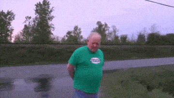 an elderly man in a green shirt is standing on the side of the road .