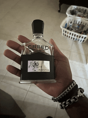 a person holding a bottle of creed aventus