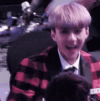 a young man with pink hair is wearing a plaid jacket and tie and smiling .
