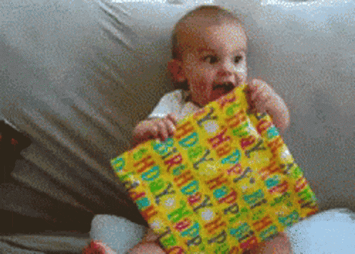 a baby is biting into a birthday present wrapped in happy birthday wrapping paper