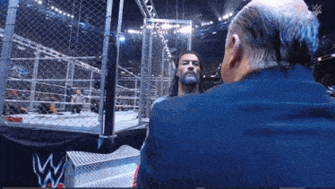 a man in a suit talks to another man in a wrestling ring with a w logo in the background