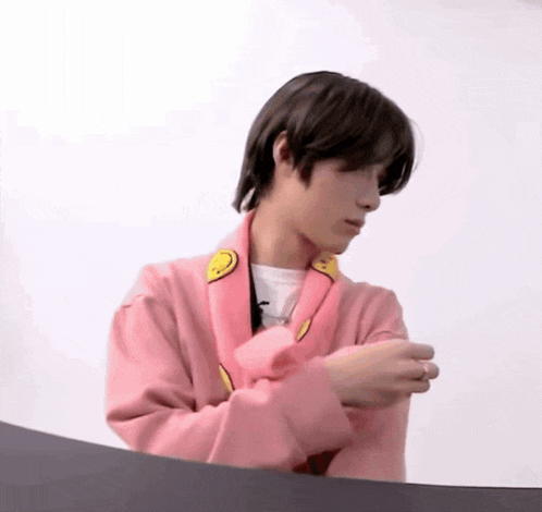 a young man wearing a pink sweater with a yellow smiley face on it is sitting at a table .