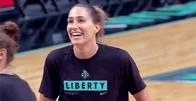 a female basketball player wearing a liberty t-shirt is smiling on the court .