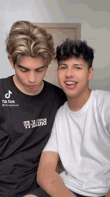 two young men are posing for a picture and one of them has a tattoo on his arm