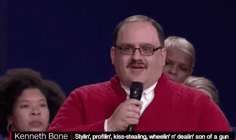a man with a mustache is holding a microphone in front of a crowd .