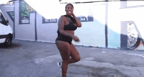 a woman in a black bra and shorts is dancing in front of a white van .