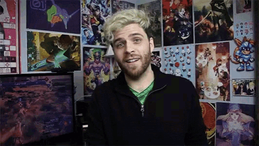 a man with blonde hair and a beard stands in front of a wall covered in posters