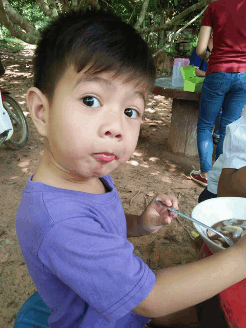 a young boy in a purple shirt holds a spoon in his mouth