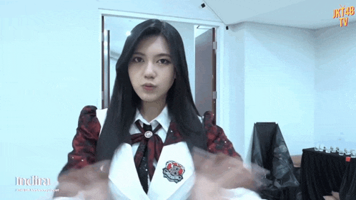 a girl in a school uniform is standing in a room with her hands folded .