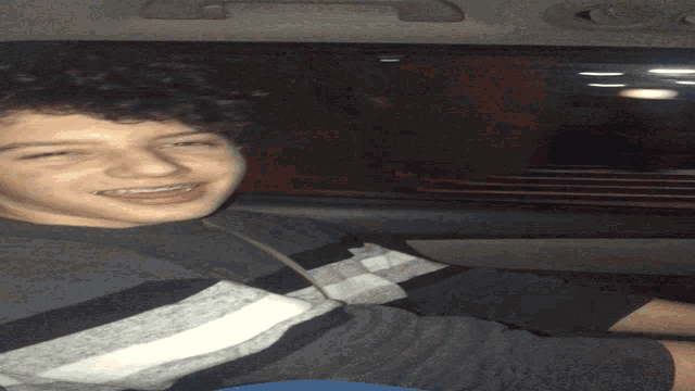a young man with curly hair is laying upside down in a car and smiling