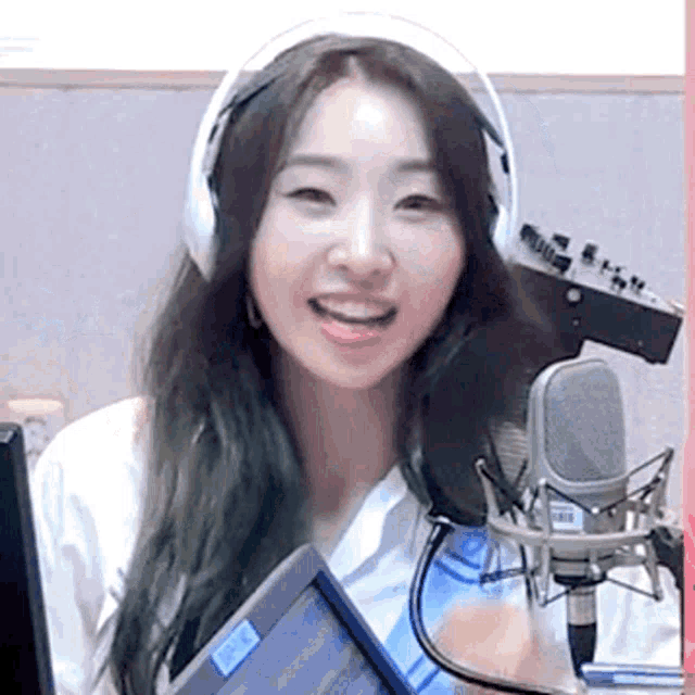 a woman wearing headphones is smiling in front of a microphone and a monitor