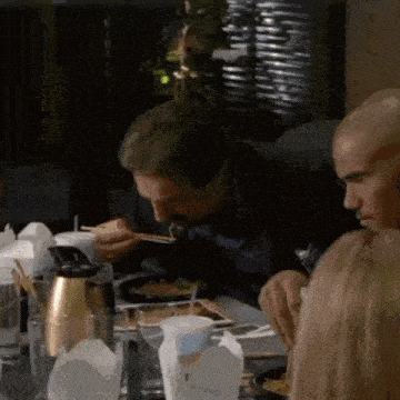 a man is eating food with chopsticks at a table with other people