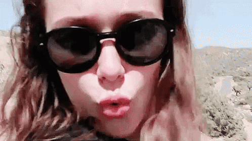 a woman wearing sunglasses and making a kiss with her lips .