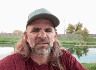 a man with long hair and a beard is wearing a hat and looking at the camera .