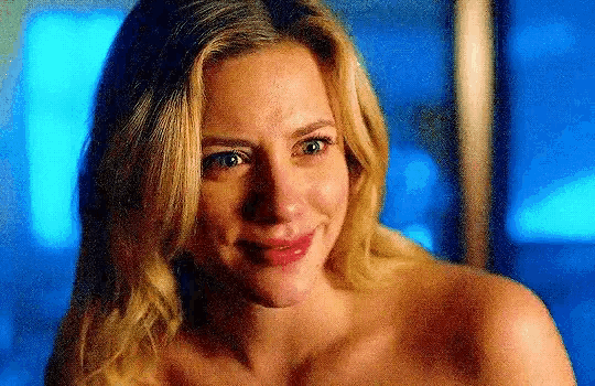a woman without a shirt is smiling and looking at the camera in a blurry photo .
