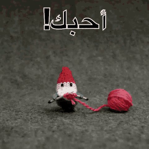a knitted gnome is holding a red heart next to a ball of yarn