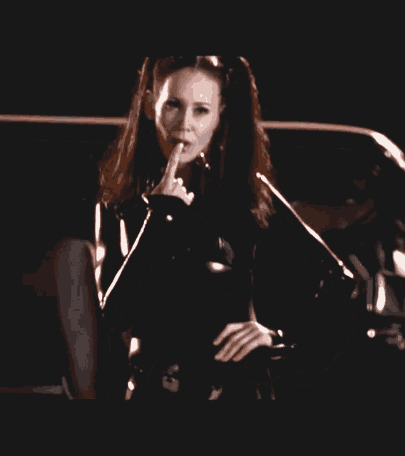 a woman in a black latex suit holds her finger to her lips