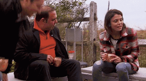 a man and a woman are sitting on a bench talking to each other while a man looks on .