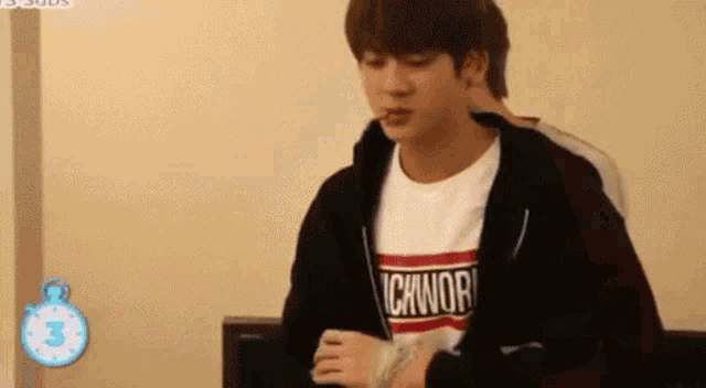 a young man wearing a black jacket and a white t-shirt is sitting on a couch with a bandaged hand .