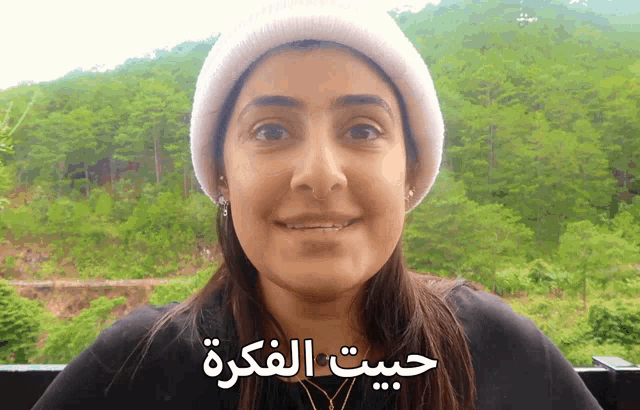 a woman wearing a white beanie is smiling with arabic writing on her face